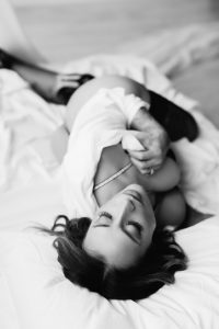 Brunette woman, laying on her back, cleavage, looking away, white shirt, laying on a bed