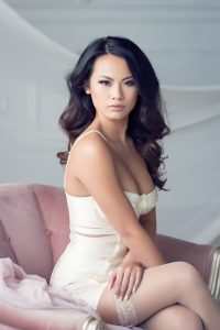 Stunning asian woman with dark brown hair in white lingerie sitting on pink chair