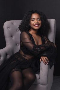 beautiful black woman in black lingerie and robe, natural curly hair and smile, sitting on grey chair