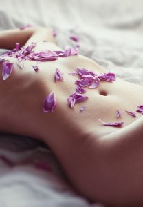 A womans body, stomach, with purple flower pedals all over her