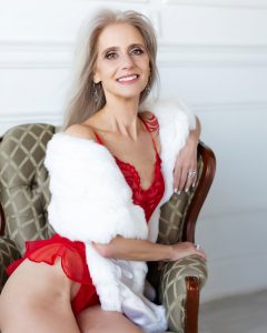 beautiful mature woman in red lingerie and fur covering smiling and sitting on vintage chair