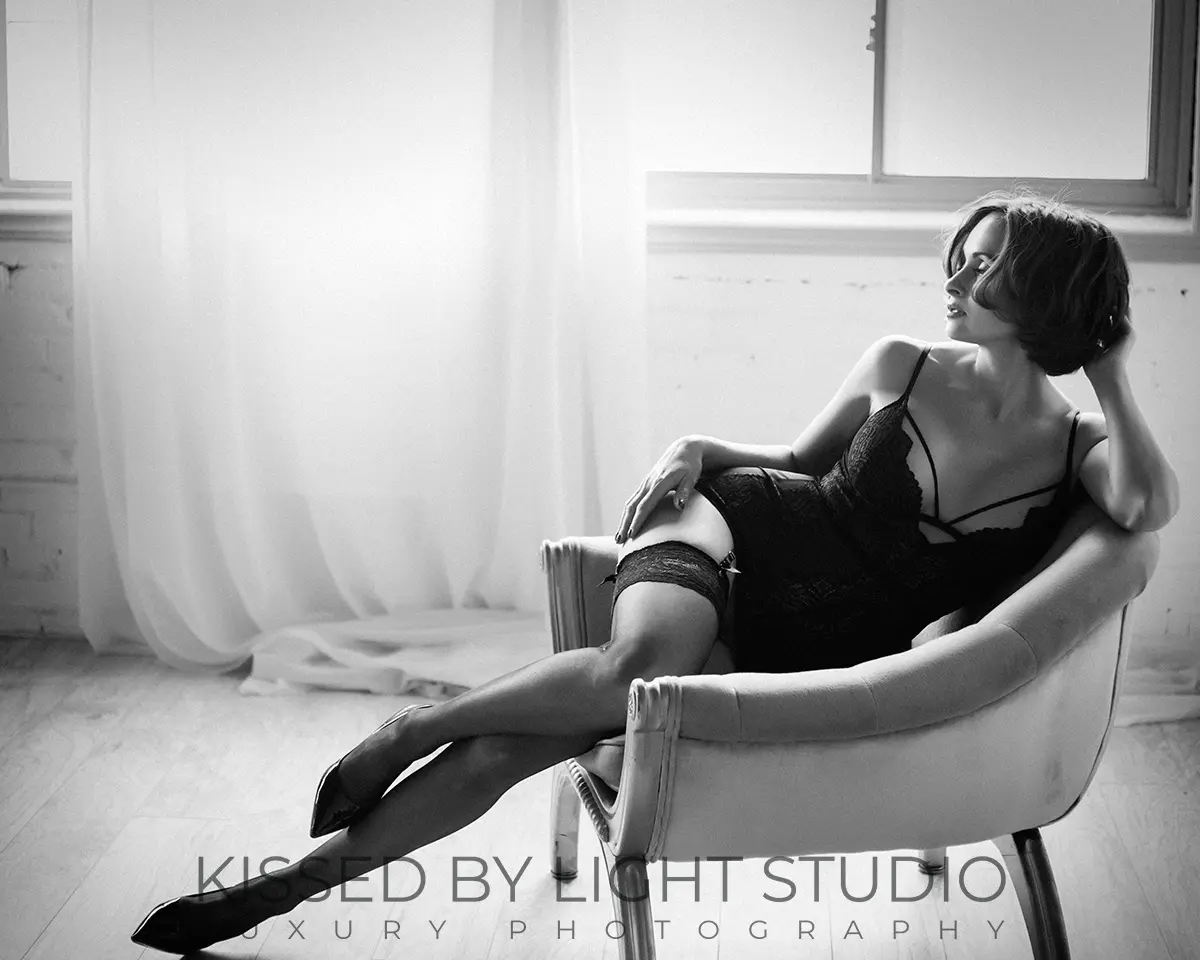 Elegant black and white boudoir portrait of a woman seated in a chair, photographed in natural light at Kissed by Light Photo Studio in Toronto